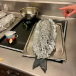Wolfsbarsch mit Kräutern gefüllt und in Alufolie luftdicht eingepackt