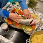 Wolfsbarsch liegt auf dem Kartoffel-Tomaten-Bett und wird mit Kräutern gefüllt