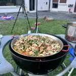Paella paella in einer Paella-Pfanne auf einem Grill fast fertig gekocht