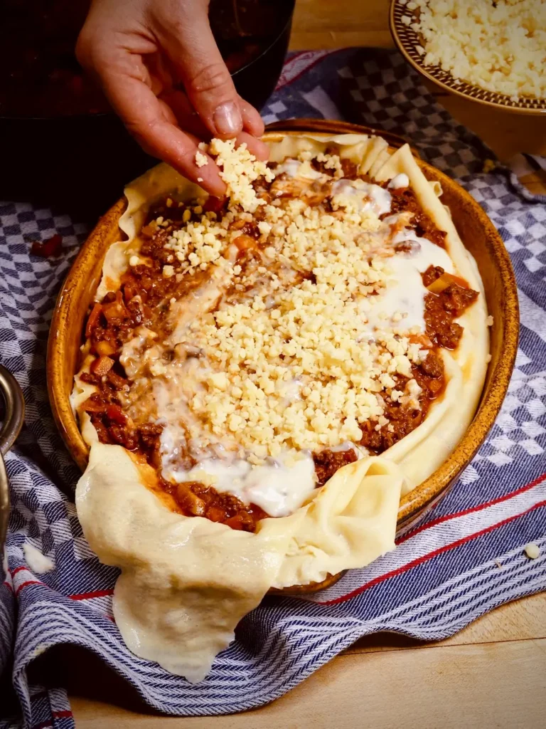 Geschichtete italienische Lasagne wird vor dem Backen mit geriebenem Parmesan bestreut