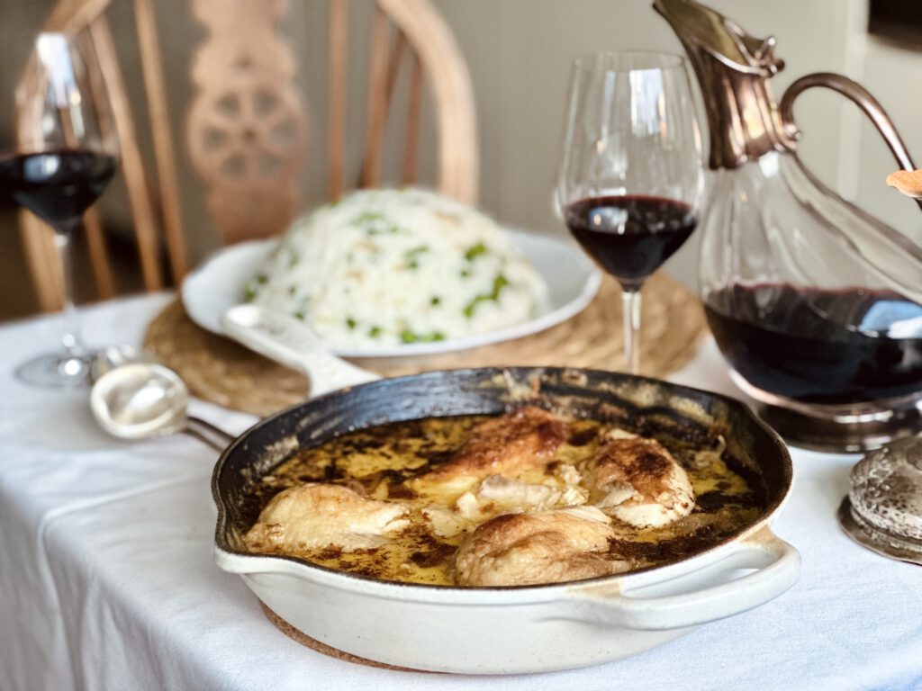 Poulet au Vin Jaune in einer Pfanne auf einem gedeckten Tisch mit Rotwein