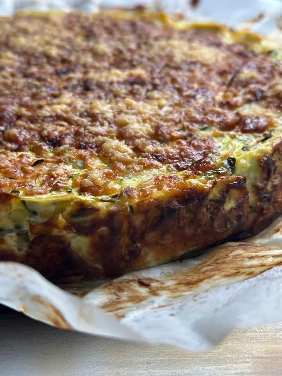Goldbraun gebackener Protein Zucchini Slice mit Halloumi und Hüttenkäse, in Stücke geschnitten auf Backpapier