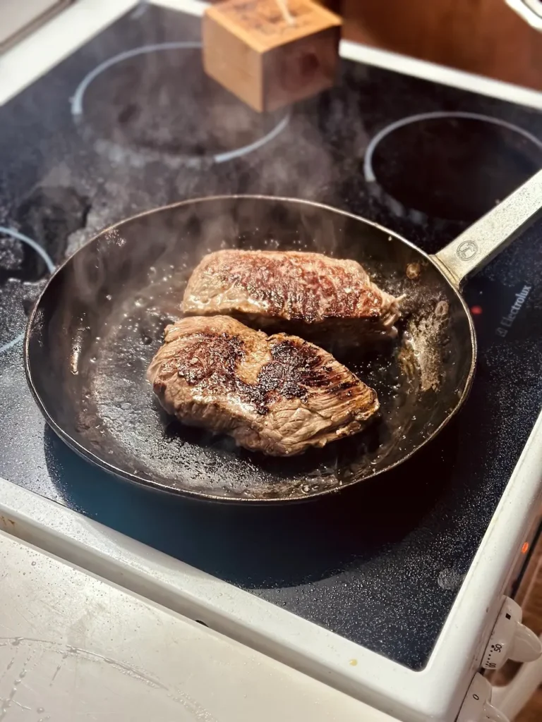 Hohrückensteak brät in einer gusseisernen Pfanne in Butter und Olivenöl