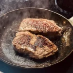 Hohrückensteak brät in einer gusseisernen Pfanne in Butter und Olivenöl