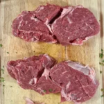 Zwei rohe Hohrückensteaks à 300 g, etwa 5 cm dick, auf einem Holzbrett