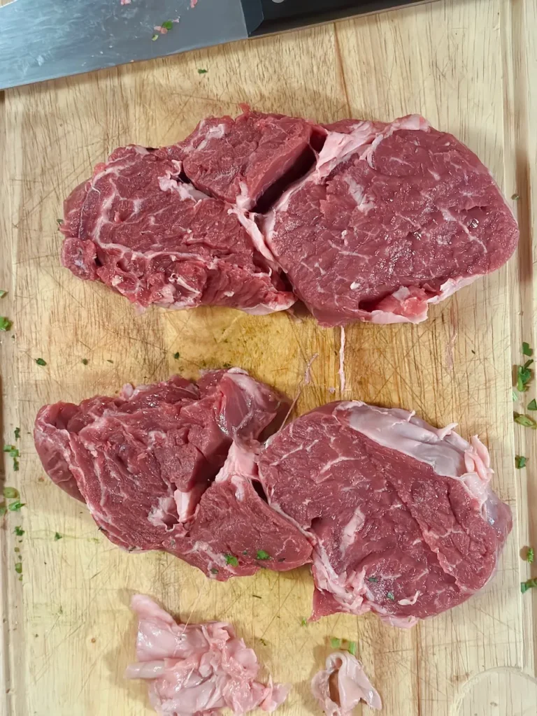 Zwei rohe Hohrückensteaks à 300 g, etwa 5 cm dick, auf einem Holzbrett