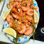 Geröstete argentinische Rotgarnelen mit Zwiebeln, Zitrone und Limette auf einem Teller, dazu Knoblauchmayonnaise